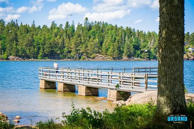 En somrig utsikt över en blå sjö vid Ursand Resort & Camping, där det klara vattnet speglas mot himlen och omgivande naturlandskap.