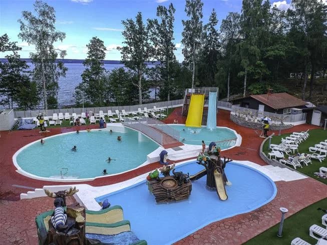 En poolområde på Ursand Resort & Camping, omgiven av solstolar och skuggande parasoller, med besökare som njuter av en avkopplande semesterdag i naturskön miljö.