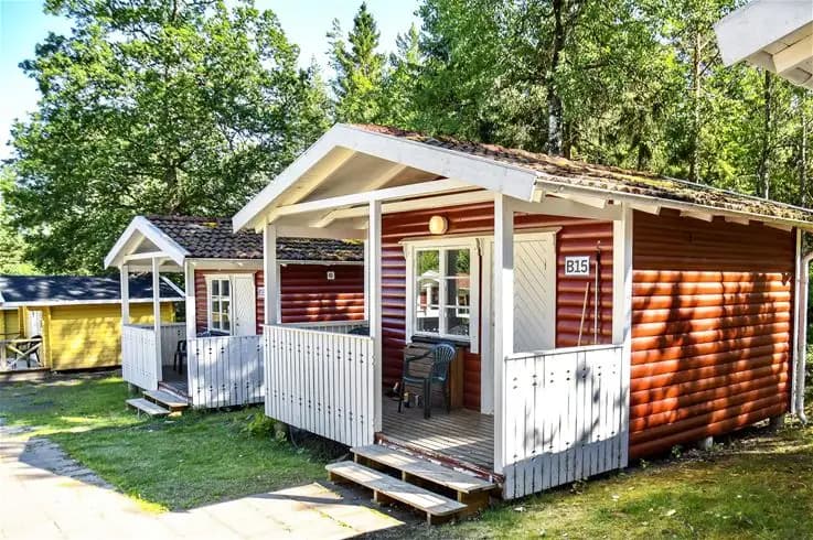 En trästuga med ljus träfasad och veranda omgiven av grönskande trädgård på Ursand Resort & Camping.