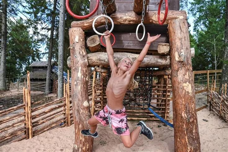 En grupp barn leker på en stor klätterställning utomhus vid Ursand Resort & Camping. De verkar ha roligt och njuta av friluftslivet under en solig dag.