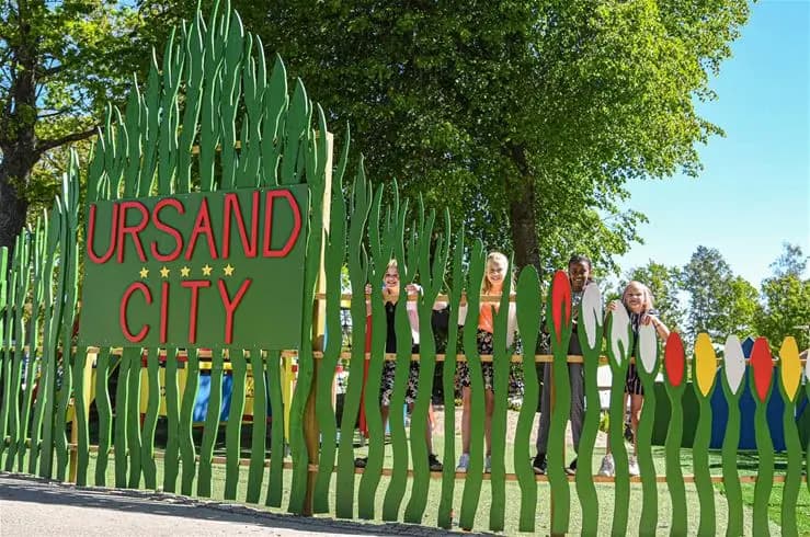 En lummig parkmiljö vid Ursand Resort & Camping med tätt grönskande buskar och vårblommor. Människor njuter av friluftslivet med gångvägar inramade av välskött trädgårdslandskap.