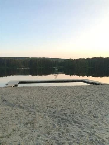 En stilla sjö vid skymning med molnreflektioner på vattnet, omgiven av lummig natur, skapar en fridfull atmosfär vid Hotings camping.