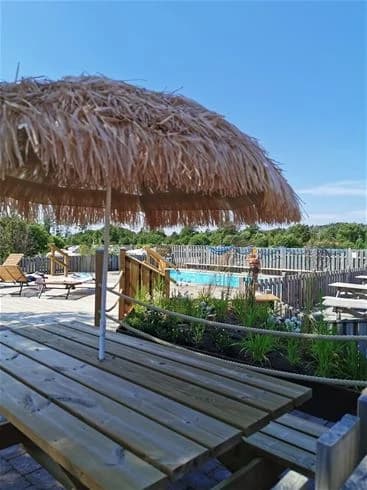 Bild av Stråvalla camping med utomhusmöbler under ett halmtak. Möblerna består av stolar och ett bord på en avskärmad veranda eller altan som ger skugga, vilket skapar en avslappnad semesterkänsla.