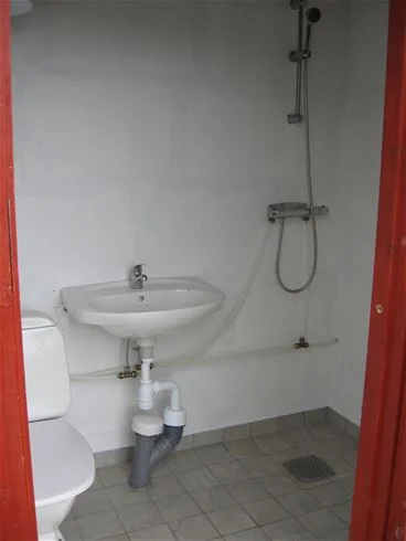 En välstädad badrumsmiljö på Stråvalla Camping, med kaklat golv och väggar, ett handfat med blandare och spegel ovanför samt modernt VVS-system.