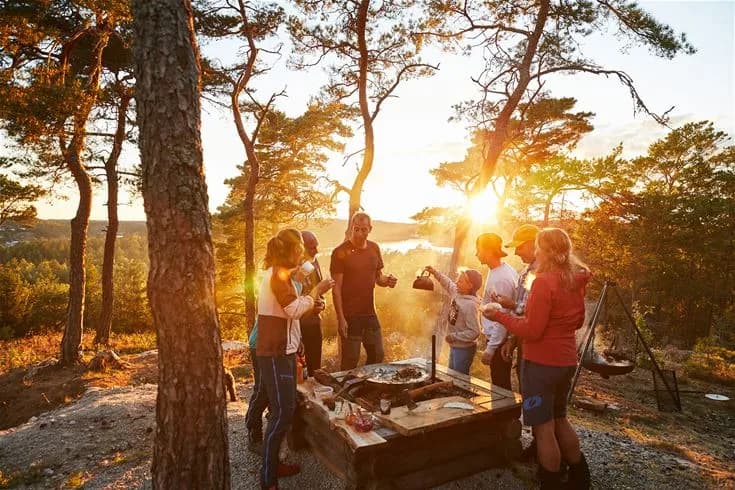 Ett tält är uppsatt vid Lagunen Camping & Stugor, där människor njuter av en solig morgon i naturen. Det finns en känsla av rekreation och gemenskap runt en picknickplats nära soluppgången.