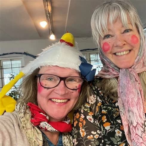 En grupp glada människor klädda i färgglada kostymer och huvudbonader samlade på Båstad camping. De ler och verkar ha roligt, med accessoarer som halsband och sjalar som en del av utstyrseln.