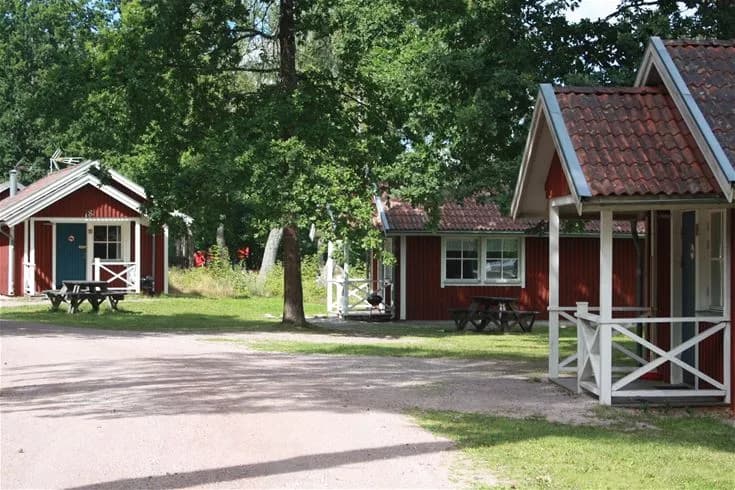 En grönskande campingplats med en stuga omgiven av träd och gräsmatta. Utomhusmöbler finns på gården, som också erbjuder skuggiga områden. Perfekt för avkoppling och rekreation.