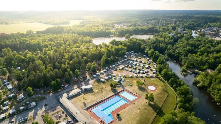 Flygfoto över Skantzö Bad & Camping visar en grönskande parkmiljö med campingområden, en stor swimmingpool och omgivande bostadsområden.