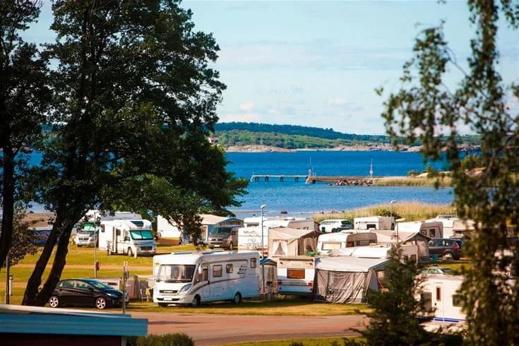 Utsikt över Lisebergs camping Askim Strand med havet i bakgrunden, en strand och en husbil i förgrunden, perfekt för en solig semester vid kusten.