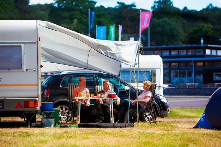 En lugn campingplats vid Lisebergs Camping Askim Strand med tält och husbilar parkerade nära varandra. I förgrunden syns en bil med öppen dörr och ett tält uppsatt intill, medan andra fordon och tält är utspridda i bakgrunden. En skön plats för utomhusaktiviteter och fritidsnöje.