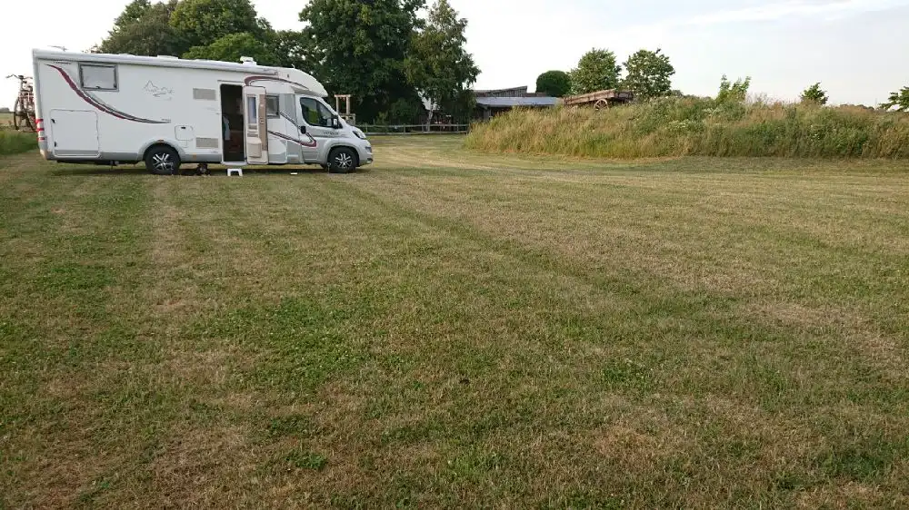 En stor gräsbevuxen äng med en parkerad husvagn på en ställplats kallad Wild West. I bakgrunden syns vidsträckta grässlätter och öppna fält.