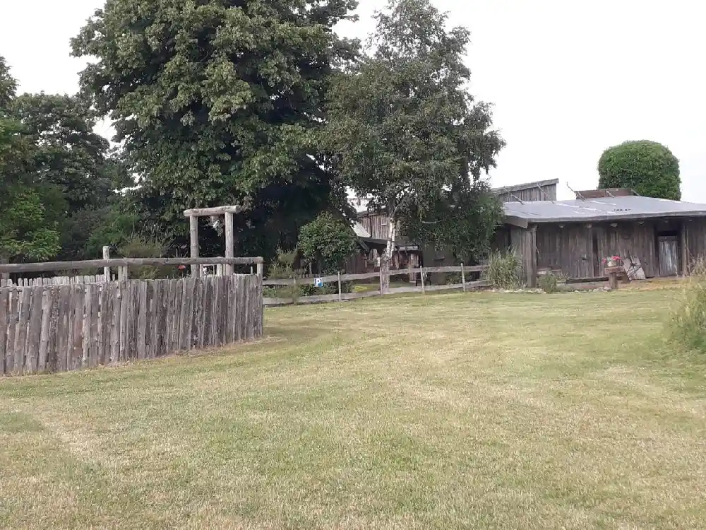 En ställplats i lantlig miljö med gröna ängar, ett staket och skuggiga områden, liknande en ranch.