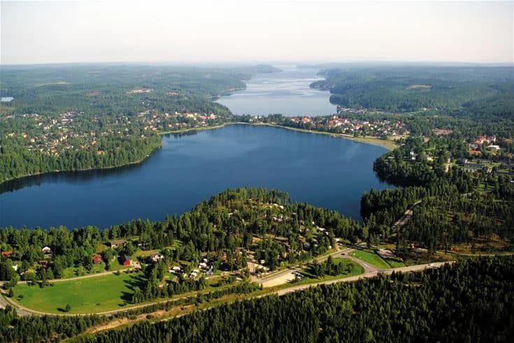 Flygbild över Gröna Backe Camping & Stugor, med en närliggande vattenresurs som en sjö eller kanal och omgivande grönskande landskap.