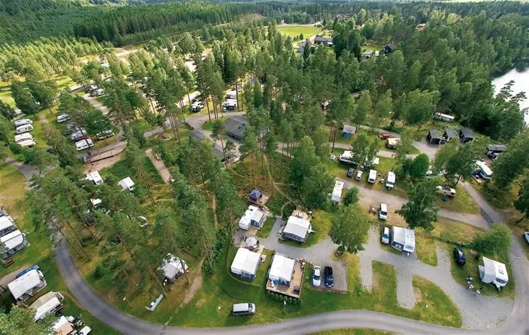 Luftfoto av Gröna Backe Camping & Stugor, visar frodig grönska med träd och växter kring campingområdet, flod slingrar sig igenom landskapet, omgiven av skog och öppna ytor.