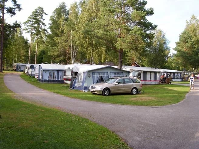 En grön campingplats med träd och gräsmatta, samt en husbil parkerad på området vid Gröne Backe Camping & Stugor.