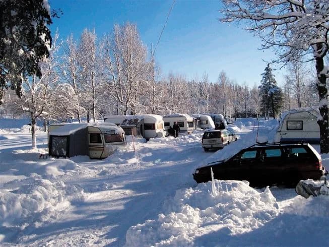 En snötäckt campingplats med parkerade bilar och stugor i vintermiljö på Gröna Backe Camping & Stugor.