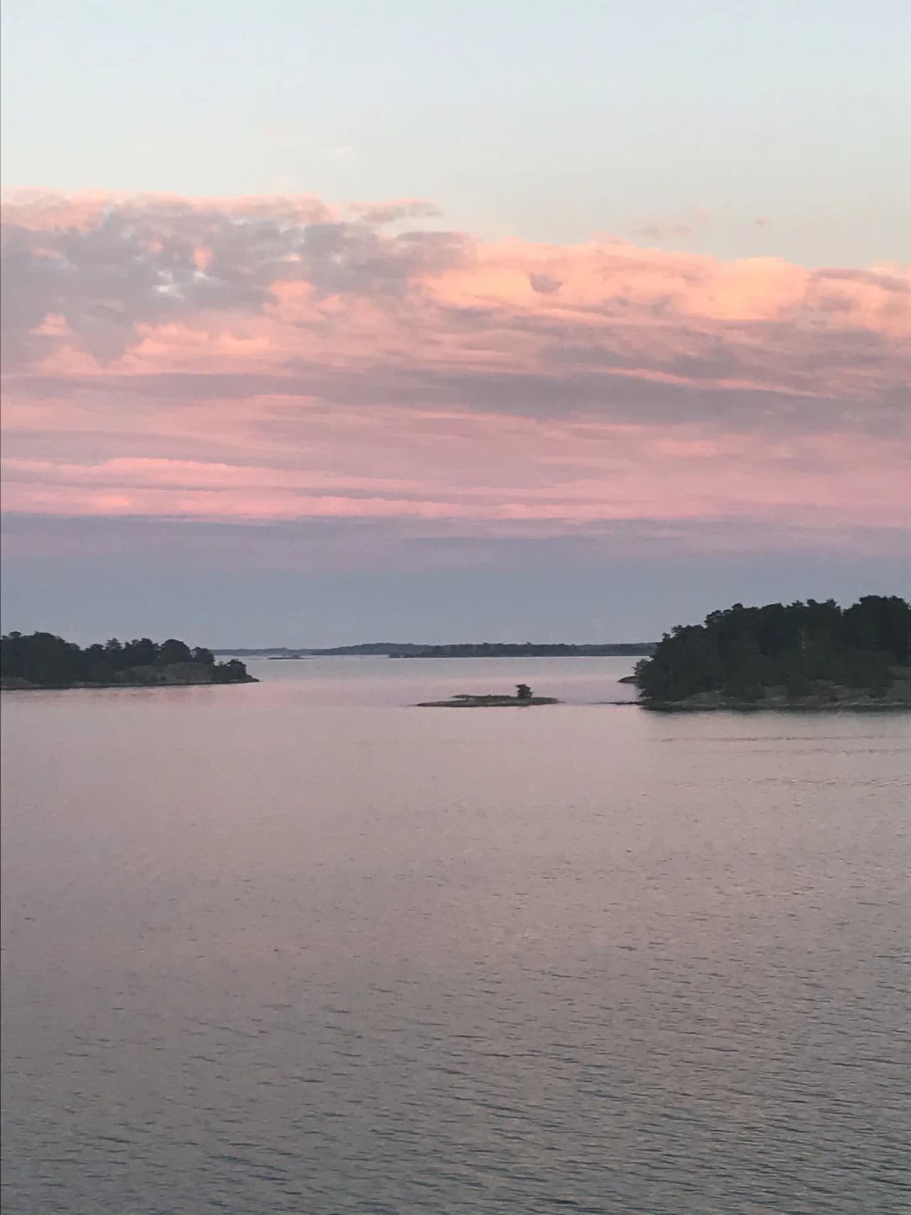 En lugn sjö vid Tyrislöt camping i skymningsljus, med en klar horisont och mjuka moln som reflekteras i vattnet.