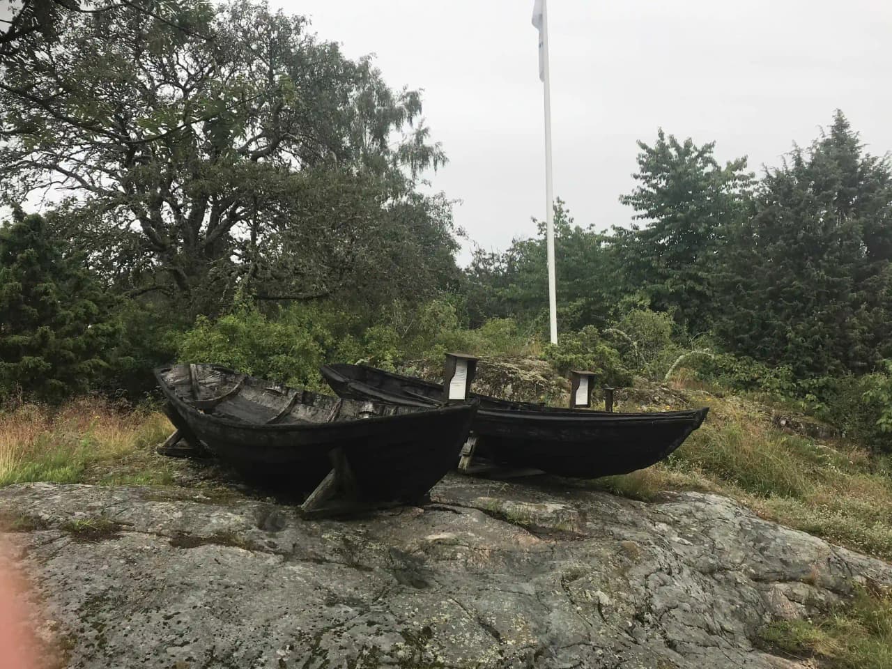 En scen vid Tyrislöt Camping med flera småbåtar och kanoter uppdragna på en klippig strand längs vattnet, omgivna av natur och sjöutsikt.