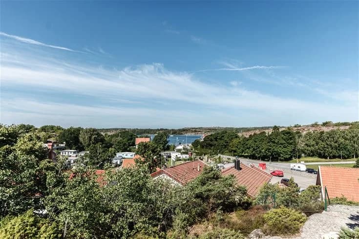 En vy över Grebbestadfjorden som visar en pittoresk by med röda tak och omgivande grönska, under en klarblå himmel. En typisk skärgårdsidyll med horisonten i bakgrunden.