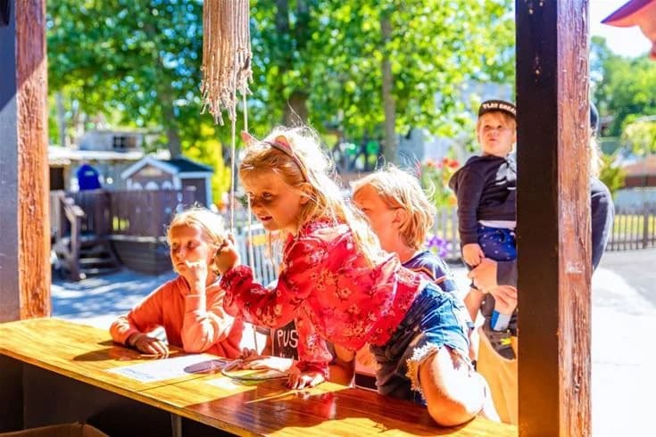 Bild av barn som leker och har roligt på Kneippbyn Resort Visby, med trälekplats och semesterstämning.