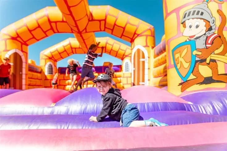 En grupp barn leker på en färgglad uppblåsbar borg vid Kneippbyn Resort Visby, omgivna av andra lekredskap och grönska i bakgrunden.