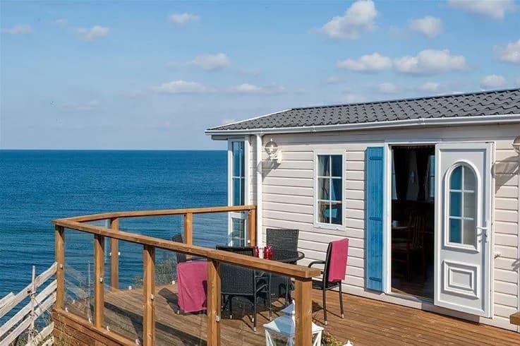 Bild av Kneippbyn Resort Visby: En kustnära vy med havet i bakgrunden. I förgrunden syns en träbalkong med stolar, som vetter mot stranden och havet.