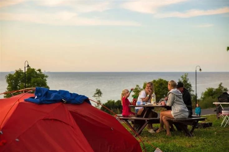 En solig sommardag vid Kneippbyn Resort Visby, där utomhusmöbler står mot en kustlinje med utsikt över havet och molnen. Perfekt för avkoppling och rekreation nära vattnet.