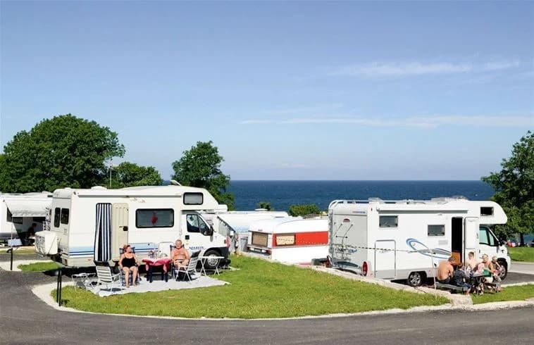 En kustnära vy från Kneippbyn Resort Visby, med havet i bakgrunden, gröna parkytor och fritidsfordon i förgrunden.