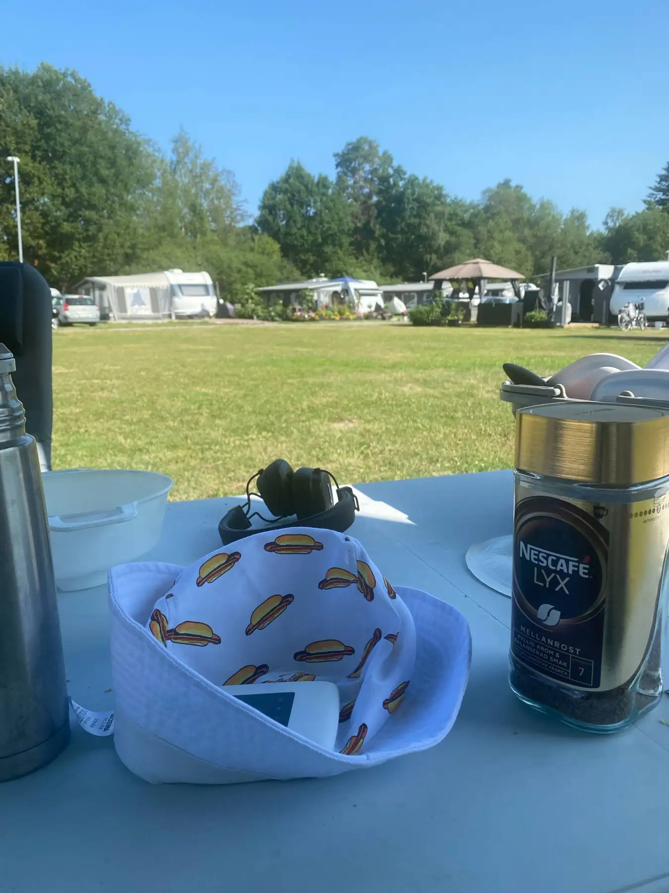 En familj på picknick vid Mälarbadens camping, sittande vid ett campingbord med solglasögon och en uppdukad måltid med tallrikar och serveringsfat.