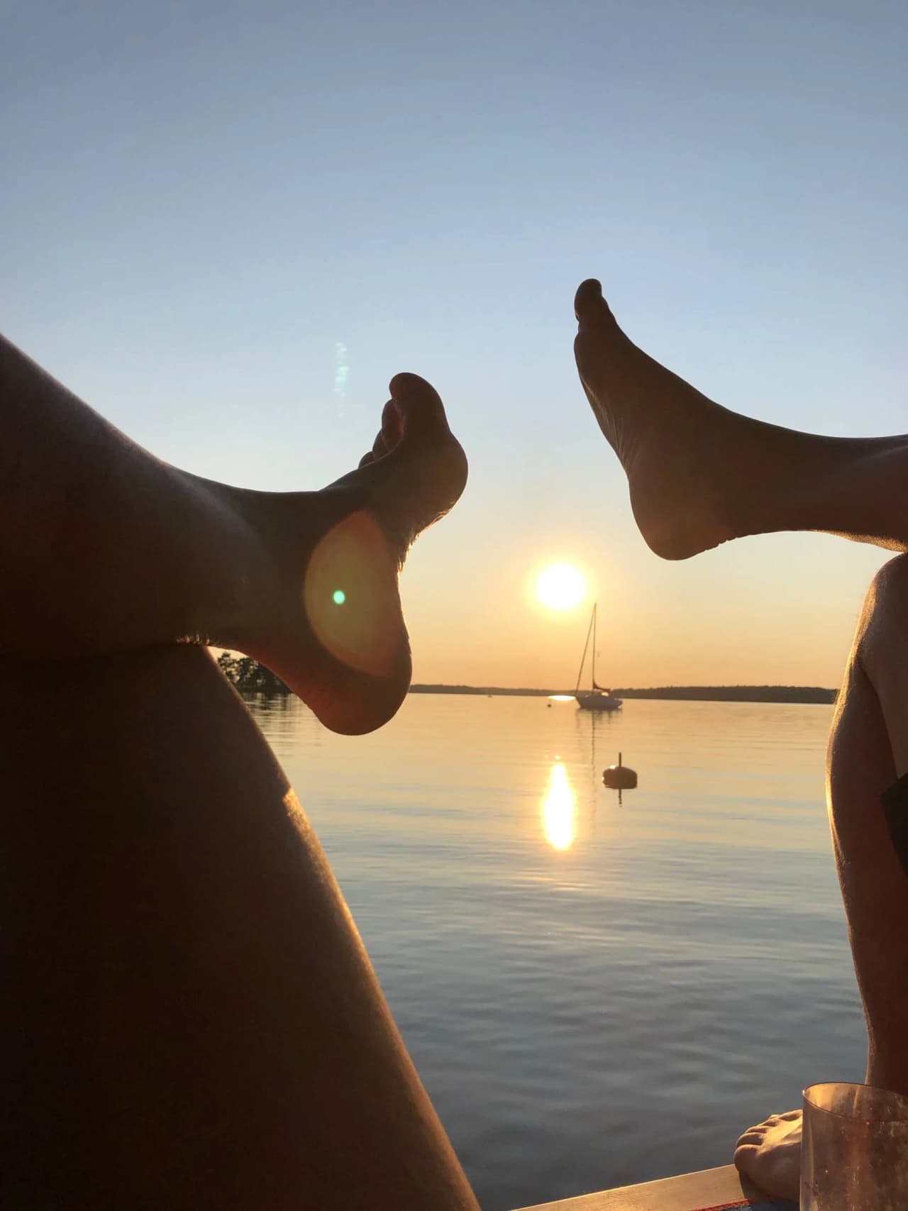 En barfotad person står vid mälarbadens strandkant i skymningen, med solens sista strålar som speglas på det lugna havet i bakgrunden.