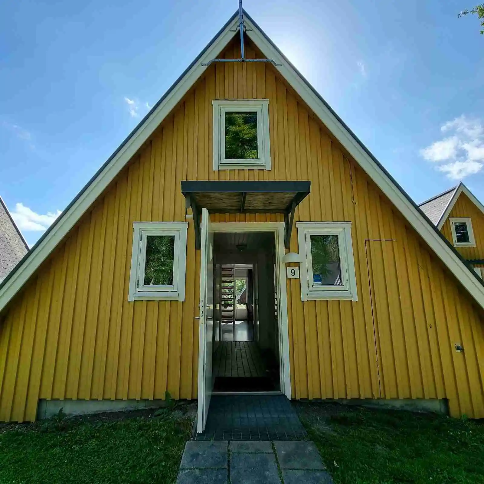 En trästuga med ett brunt tak och vitmålade plankor, omgiven av en välskött trädgård vid Mötesplats Borstahusen.