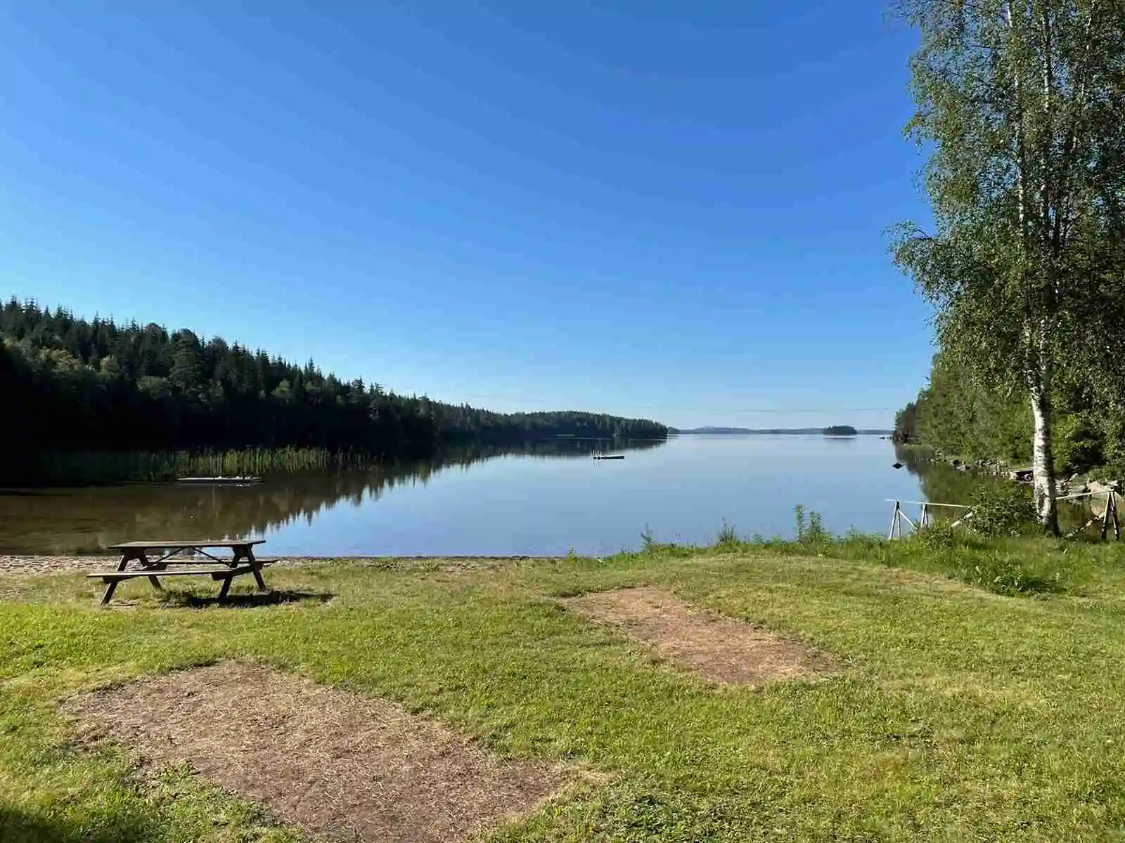 En naturskön miljö vid Sandviken fribad och camping, med en sjö omgiven av grönskande ängar och träd.