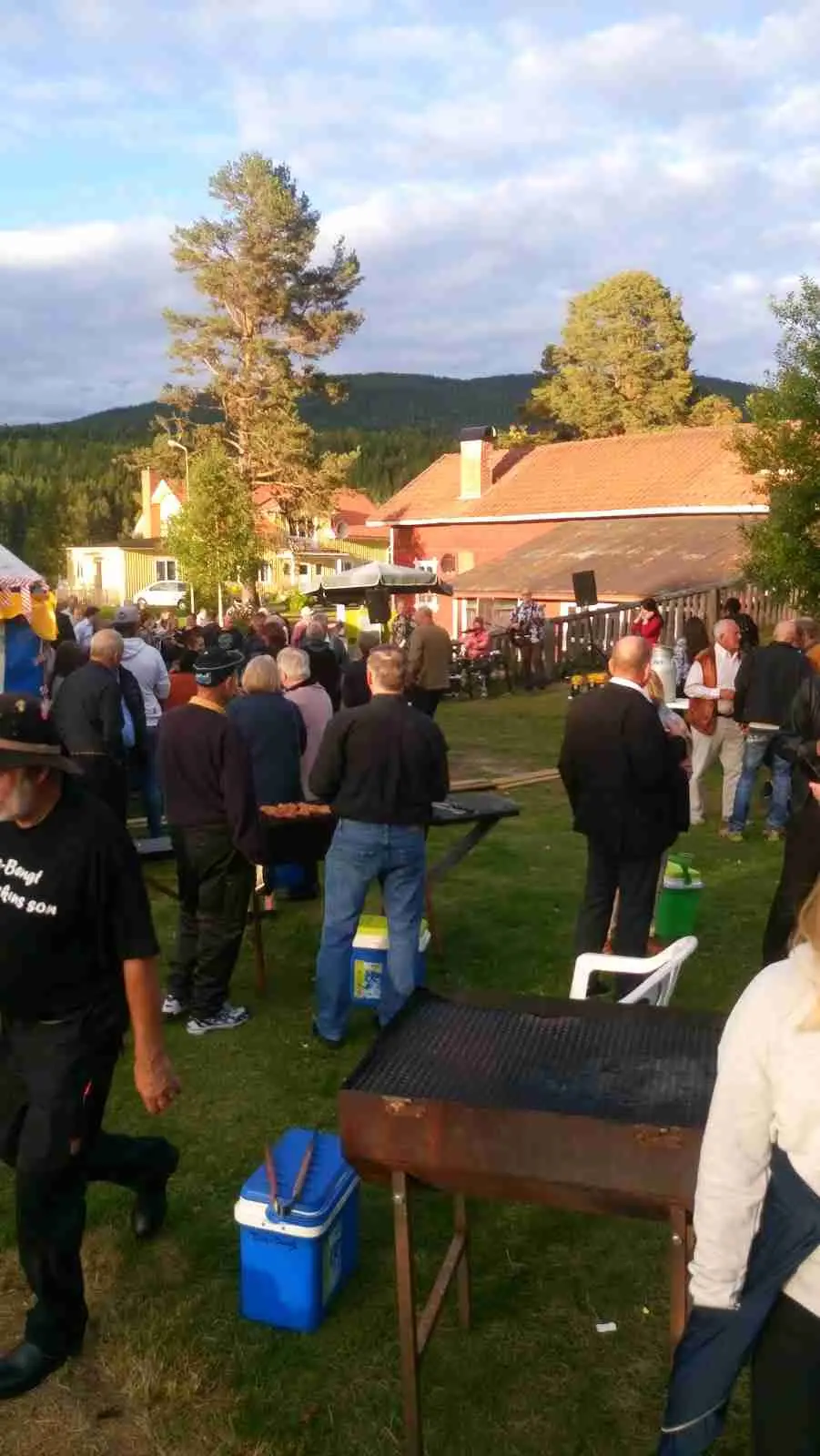 En grupp människor njuter av fritiden på Höljes Camping. De sitter på stolar utomhus i en gemytlig atmosfär, omgivna av grönska och soligt väder.