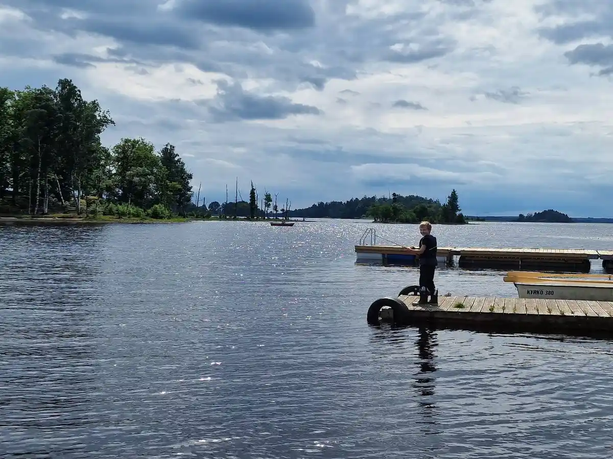 En fridfull sjö med molnig himmel, omgiven av grönska vid E4:ans camping, perfekt för rekreation och avkoppling.