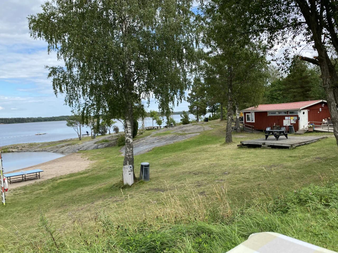 En grönskande campingplats vid vattnet med gräsmatta och kustlinje.