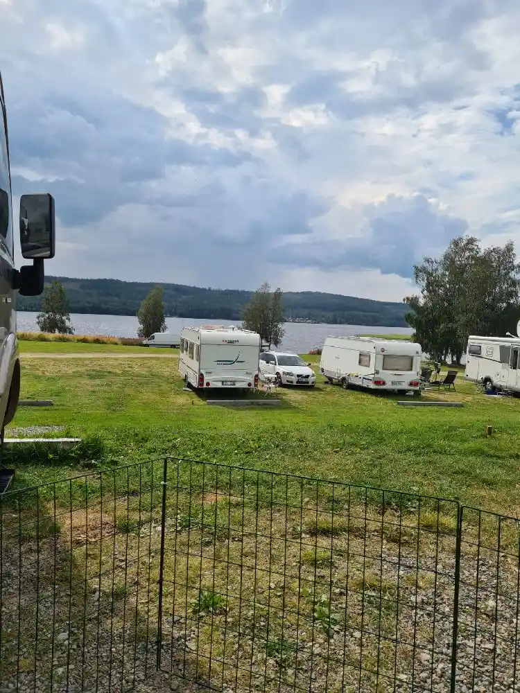 En husvagn parkerad nära en sjö i ett naturskönt område med moln på himlen, vid Rätans camping.