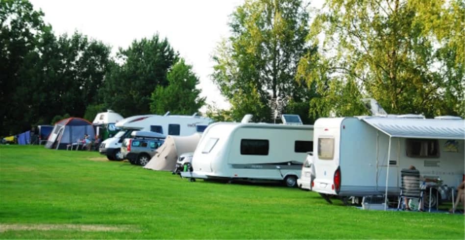 En campingplats med husvagnar, tält och gröna gräsmattor.