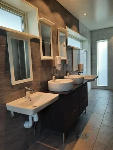 En välstädad badrumsmiljö på Vallsnäs Camping med ett modernt handfat, spegel och brun golvbeläggning.