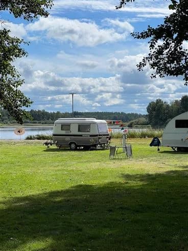 En campingplats i Hultsfred med husbilar och husvagnar uppställda på en grön gräsmatta, omgivna av tält och parkmiljö.