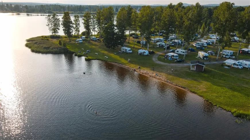 En vacker campingplats vid en sjö med grönskande omgivningar och en sandstrand. Perfekt för rekreation och avkoppling i naturen.