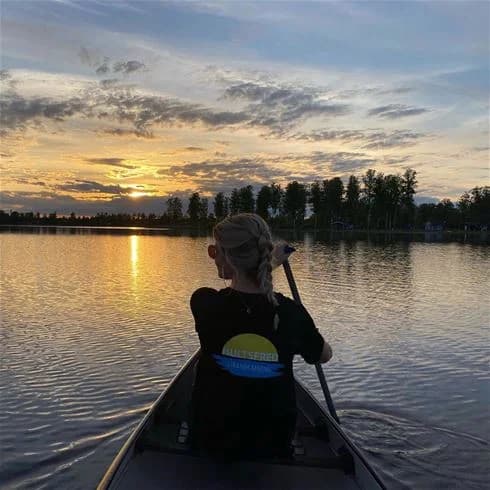 Bild av Hultsfred strandcamping vid sjö vid skymning. Flera båtar ligger förtöjda vid stranden, omgivna av stilla vatten som reflekterar en molnig himmel. Perfekt för utomhusaktiviteter och avkoppling i vacker natur.