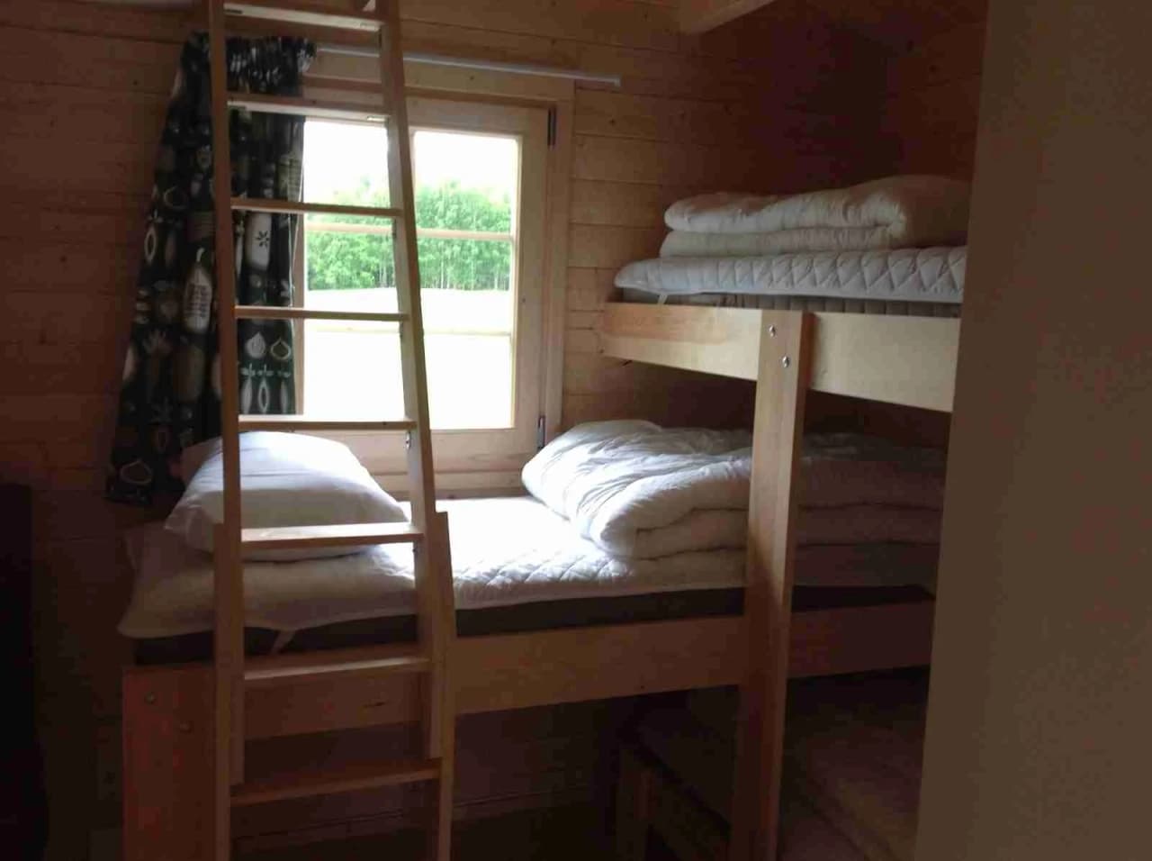 Alt-text: "Interiör av en stuga på Camping Alevi med våningssäng i trä och trägolv."