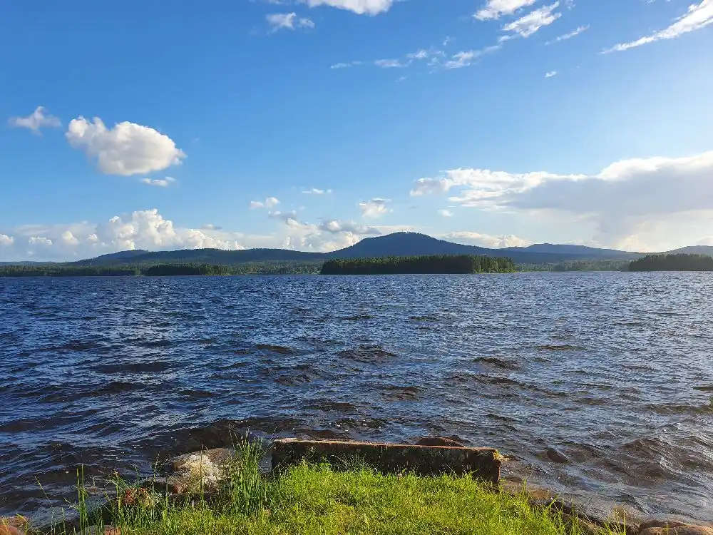 En lyxig campingplats omgiven av klarblått vatten och storslagna bergslandskap under en klarblå himmel med några vita moln.