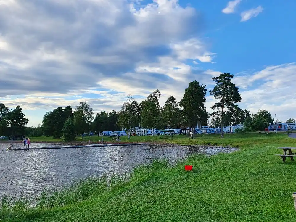 En naturskön campingplats vid en sjö med cumulusmoln på himlen. Perfekt för friluftsaktiviteter och avkoppling i naturen.