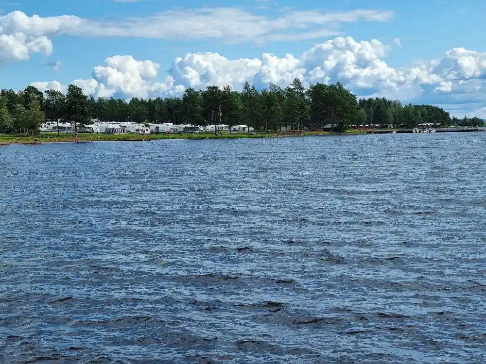 En somrig dag vid Sollerö Camping med blå himmel och moln där en vattenkälla sträcker sig över horisonten.