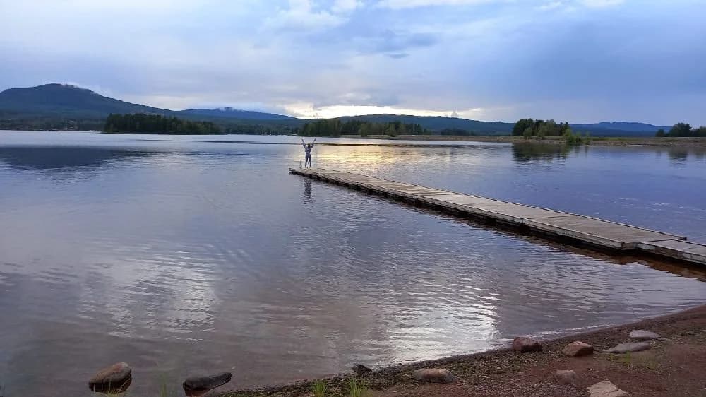 En stilla sjö med reflekterande vatten omgiven av grönskande natur och en molnig himmel vid Sollerö camping.