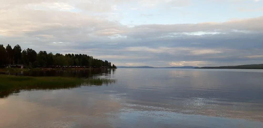 En naturskön campingplats vid vatten, med utsikt över en blå himmel och vita moln i horisonten.
