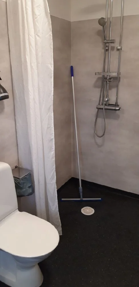 En campingtoalett utrustad med dusch, toalettstol och duschdraperi, med ett kaklat golv.