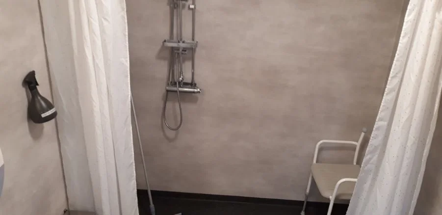 Bild av ett modernt badrum på Sollerö Camping med grå golv- och väggplattor, en silverfärgad dusch och andra VVS-inredningar.