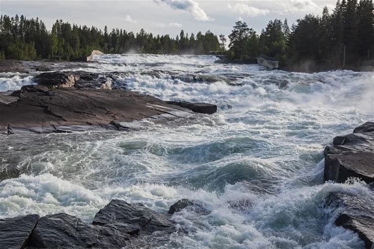 En vy över Storforstens camping, med en brusande bergsflod som strömmar genom orörd vildmark. Vattnets kraft skapar forsar bland gröna skogar och stenar. En naturskön och fridfull plats som lockar besökare för äventyr och avkoppling.
